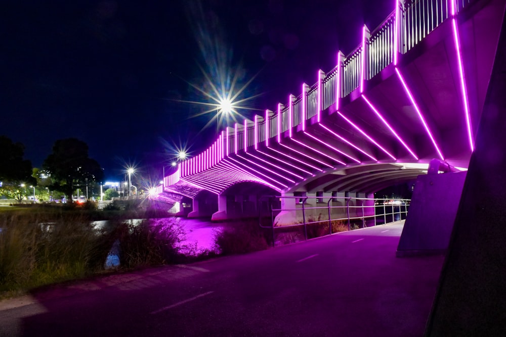 a purple lit bridge over a river at night