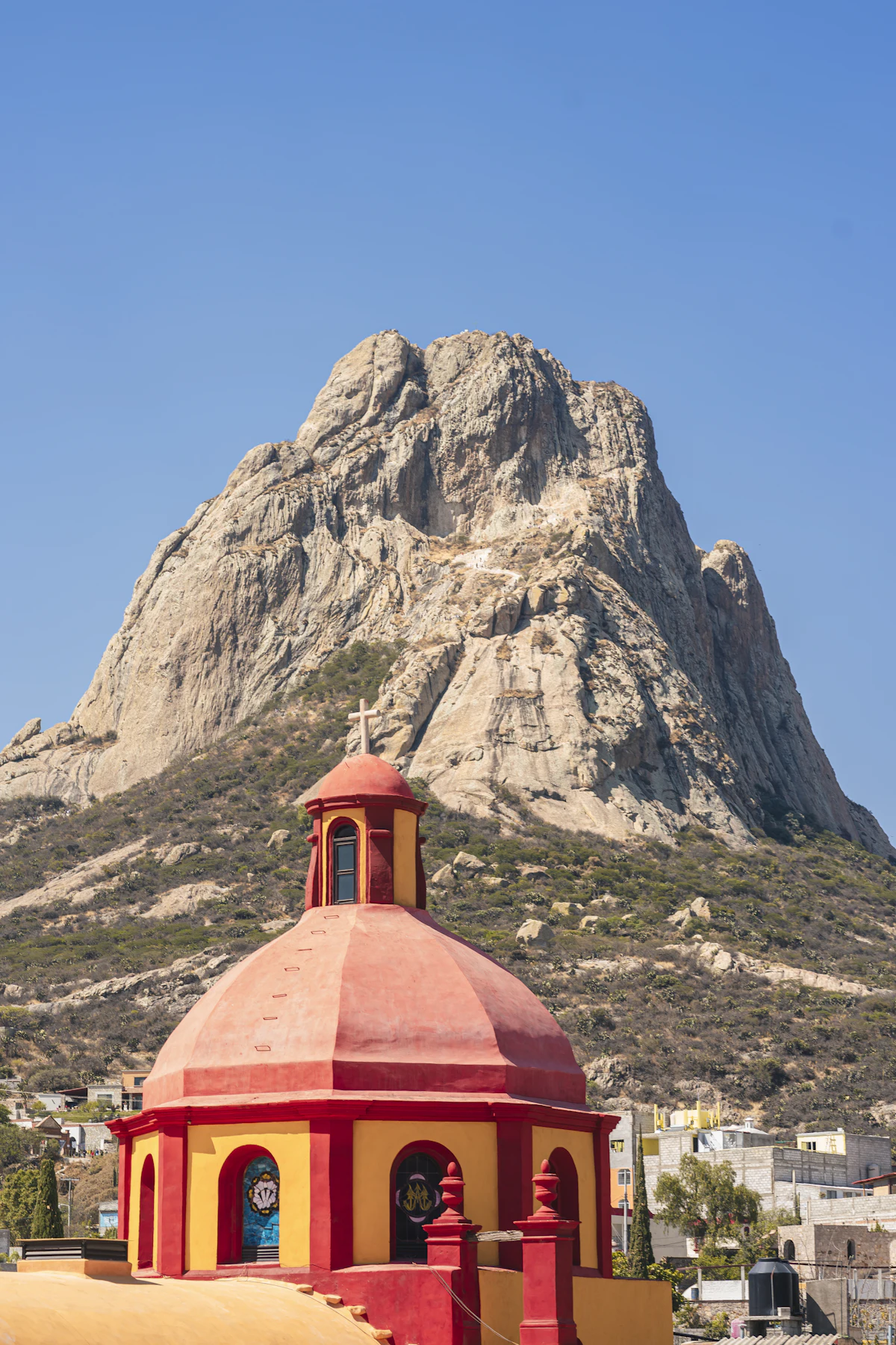 A red and yellow church dome in Bernal, with the rock of the Peña de Bernal behind it