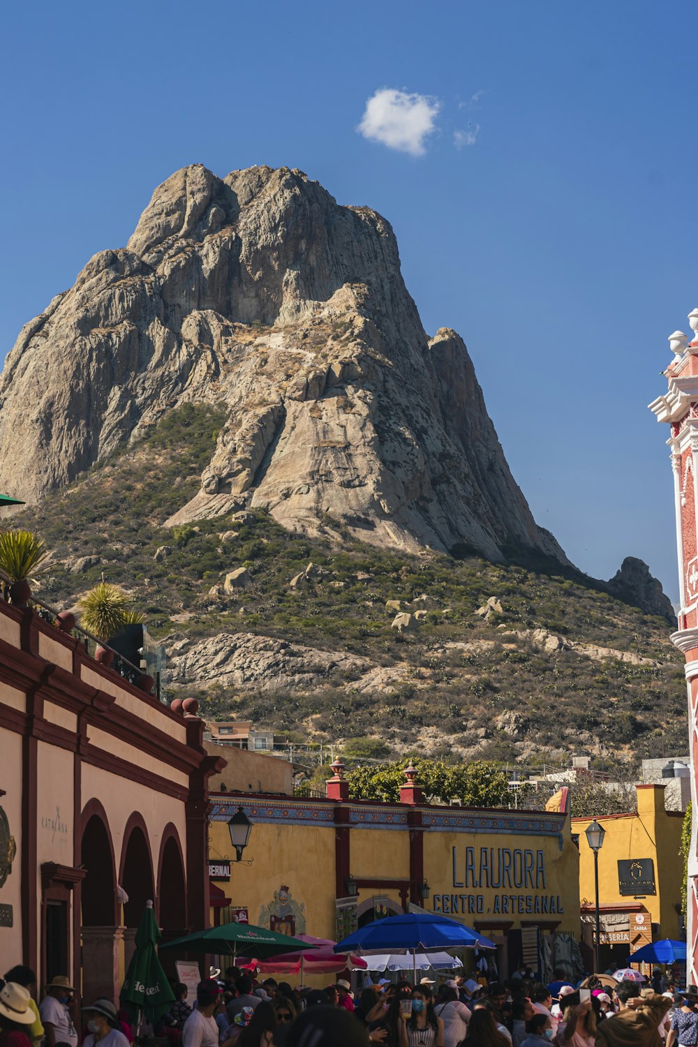 a crowd of people standing around a building with a mountain in the background