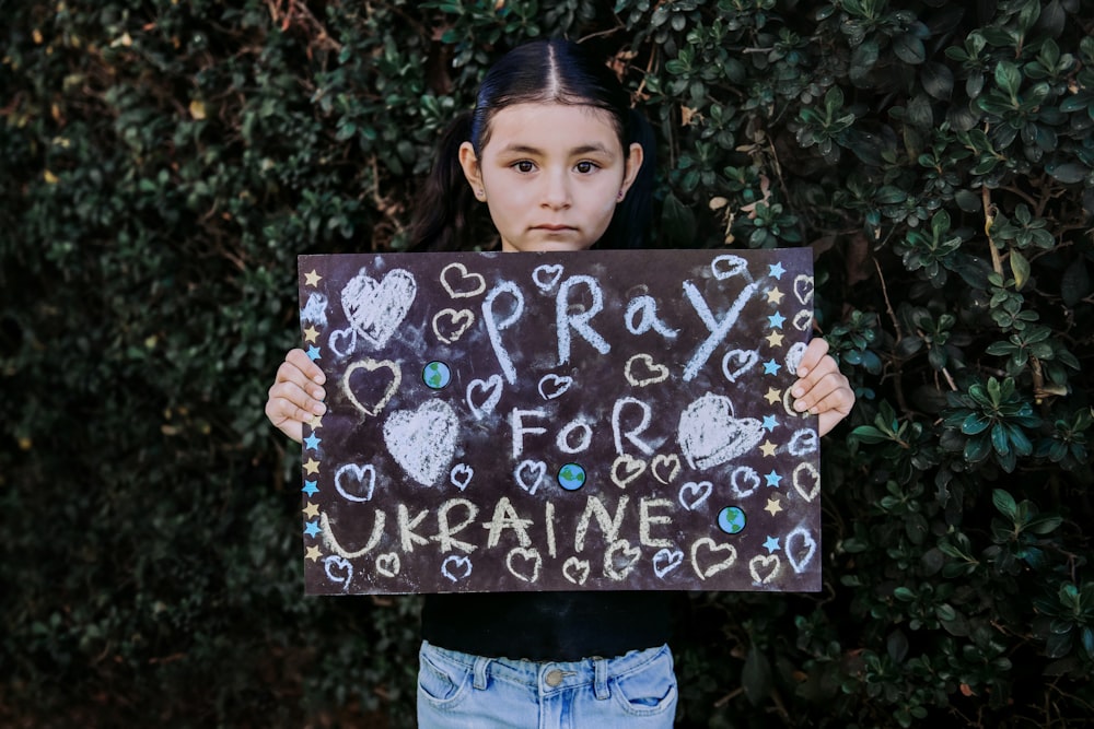 a girl holding a sign that says pray for ukraine