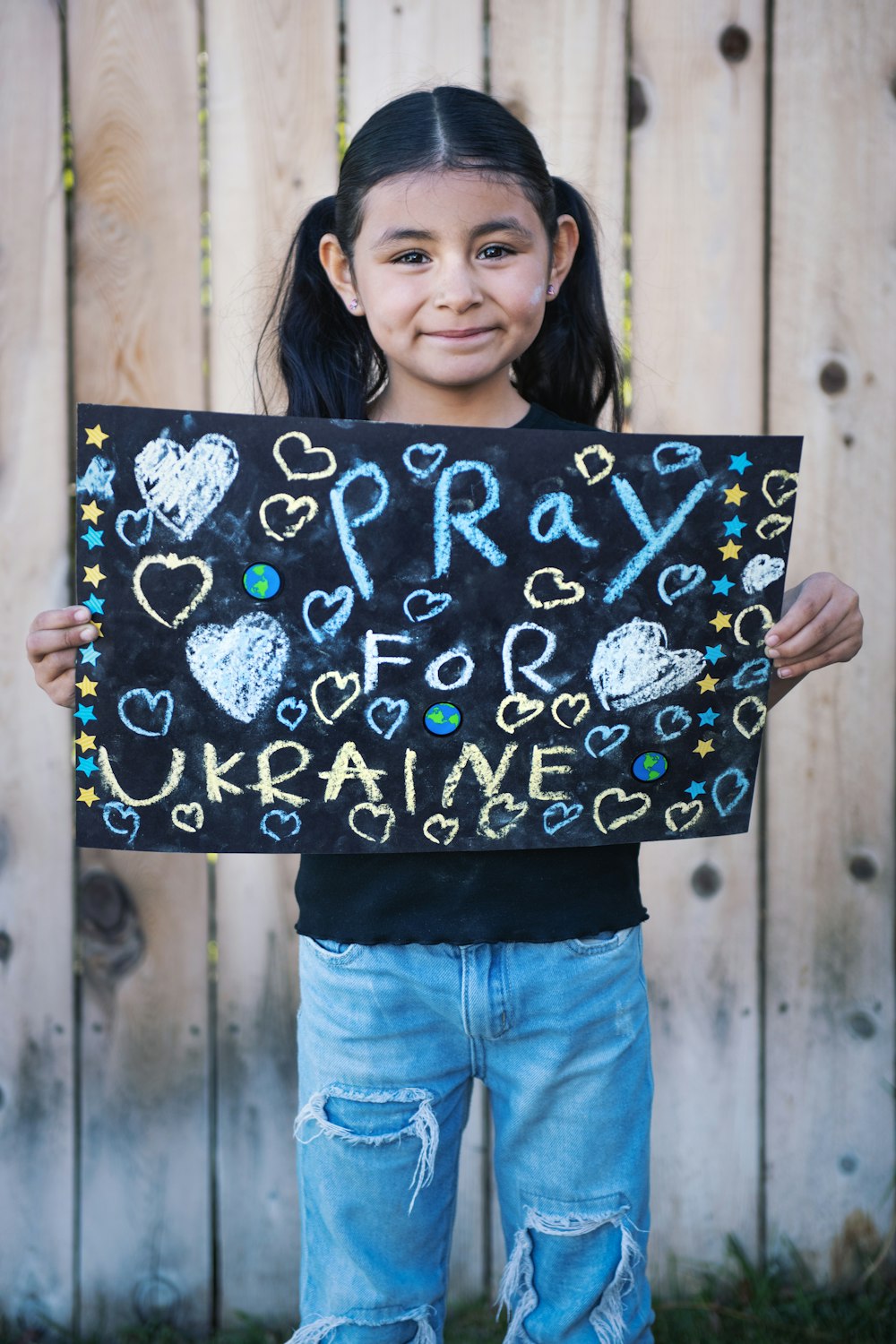 a little girl holding a sign that says pray for ukraine