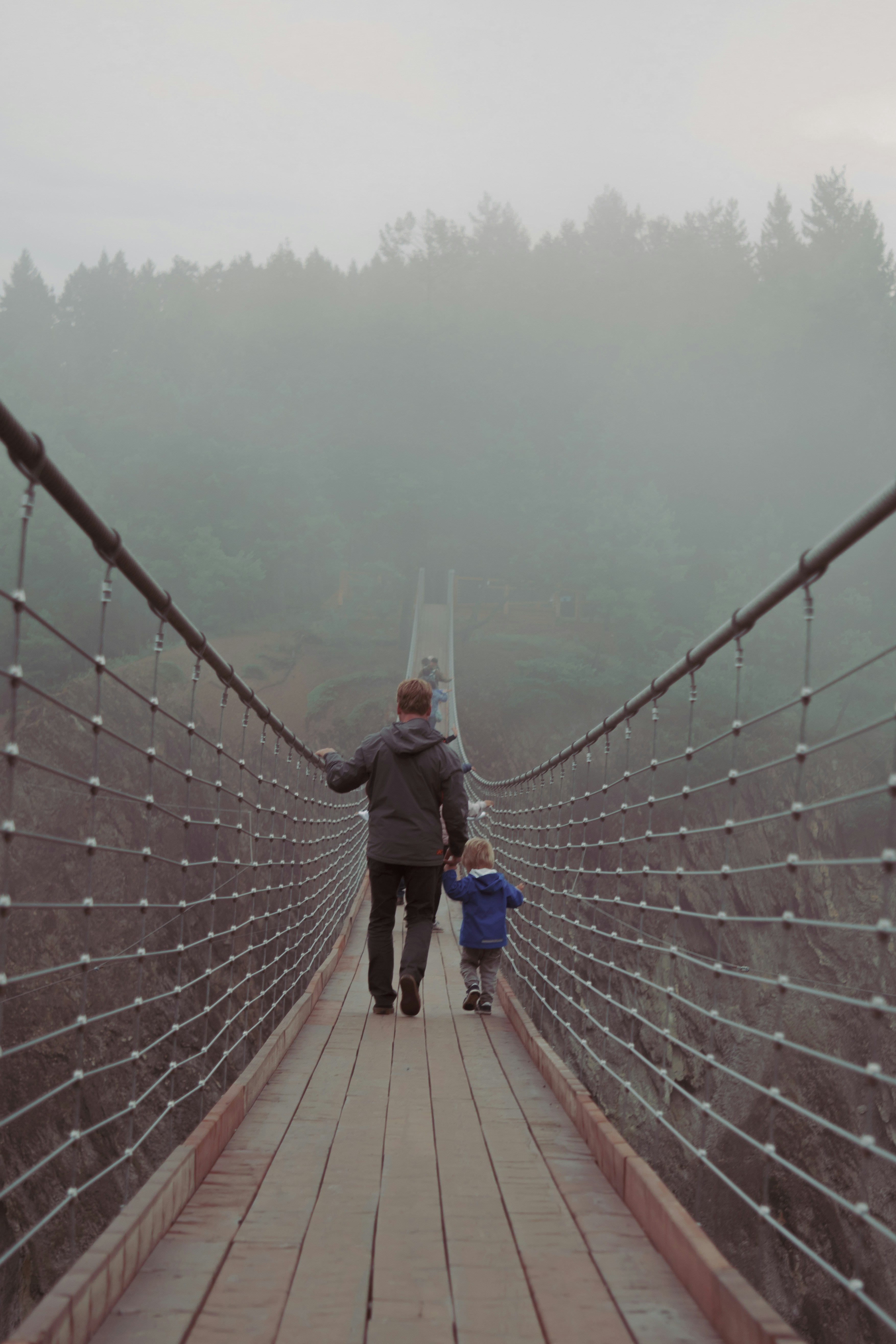 a man and a child walking across a suspension bridge