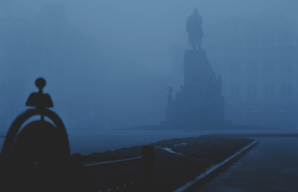 a person standing in front of a statue on a foggy day