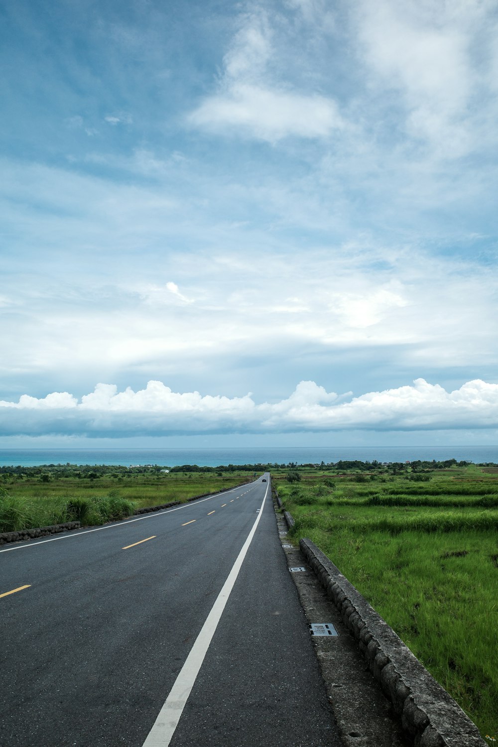 an empty road in a green field under a blue sky