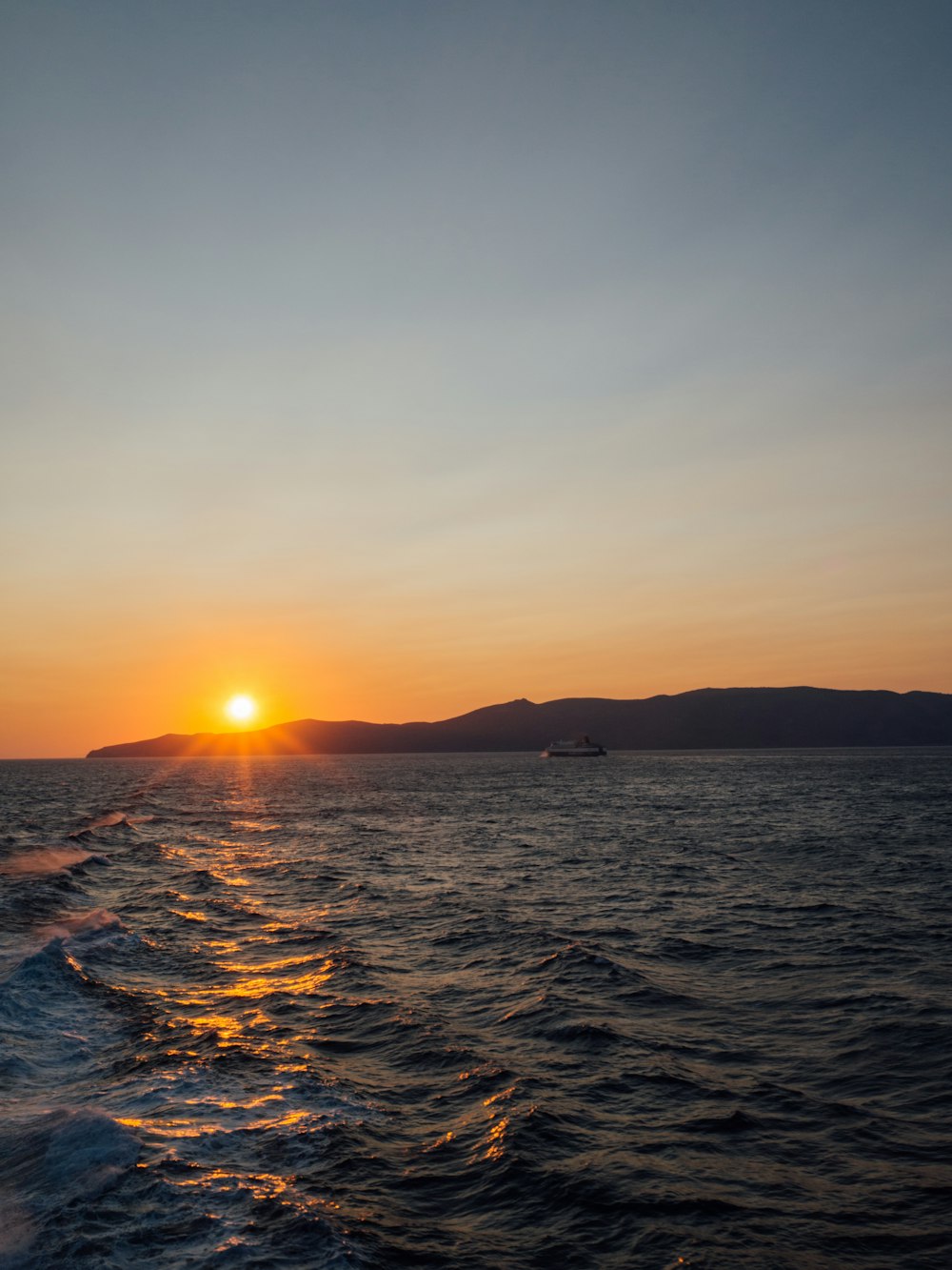 Il sole sta tramontando sull'oceano con una barca in lontananza