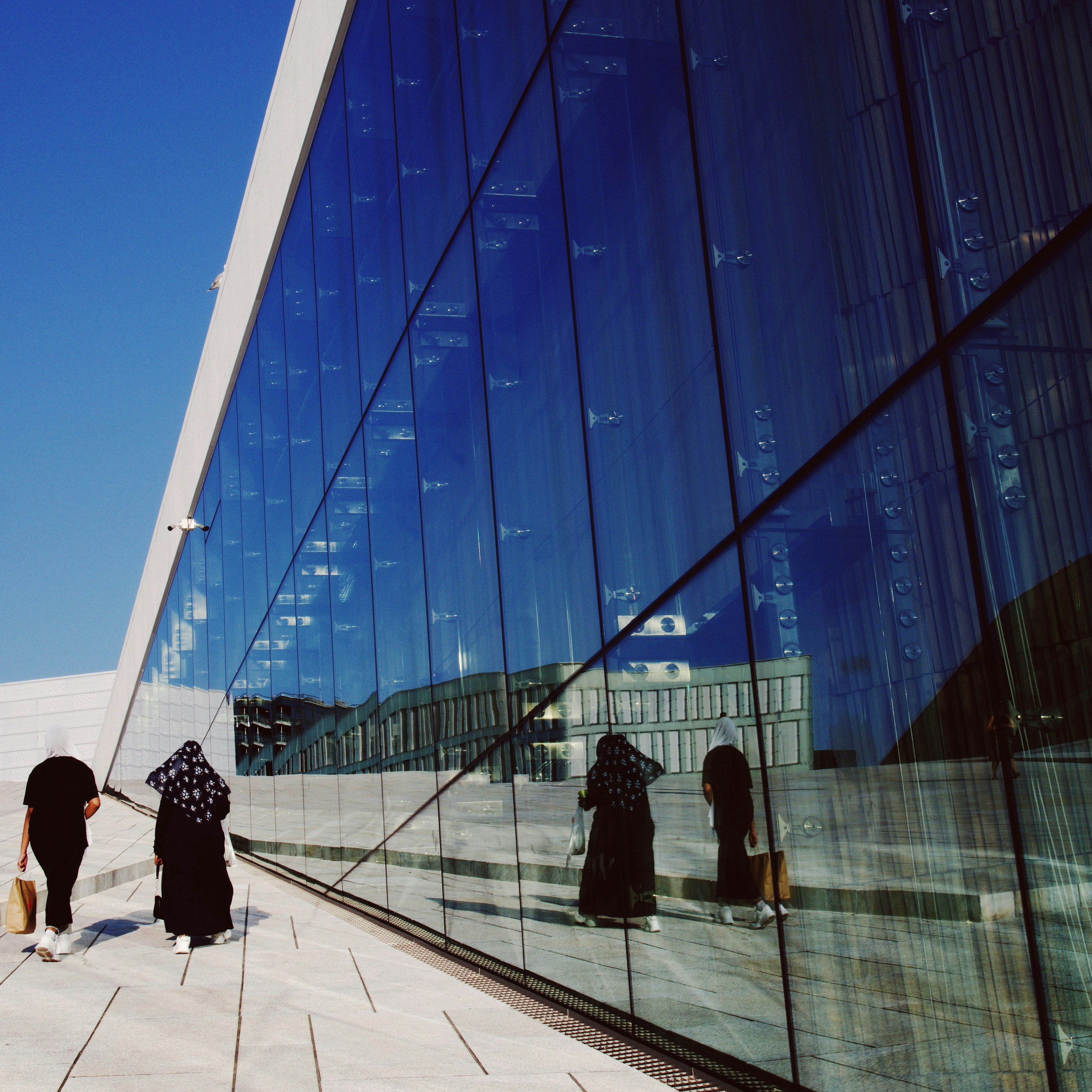 a group of people walking down a sidewalk next to a tall building