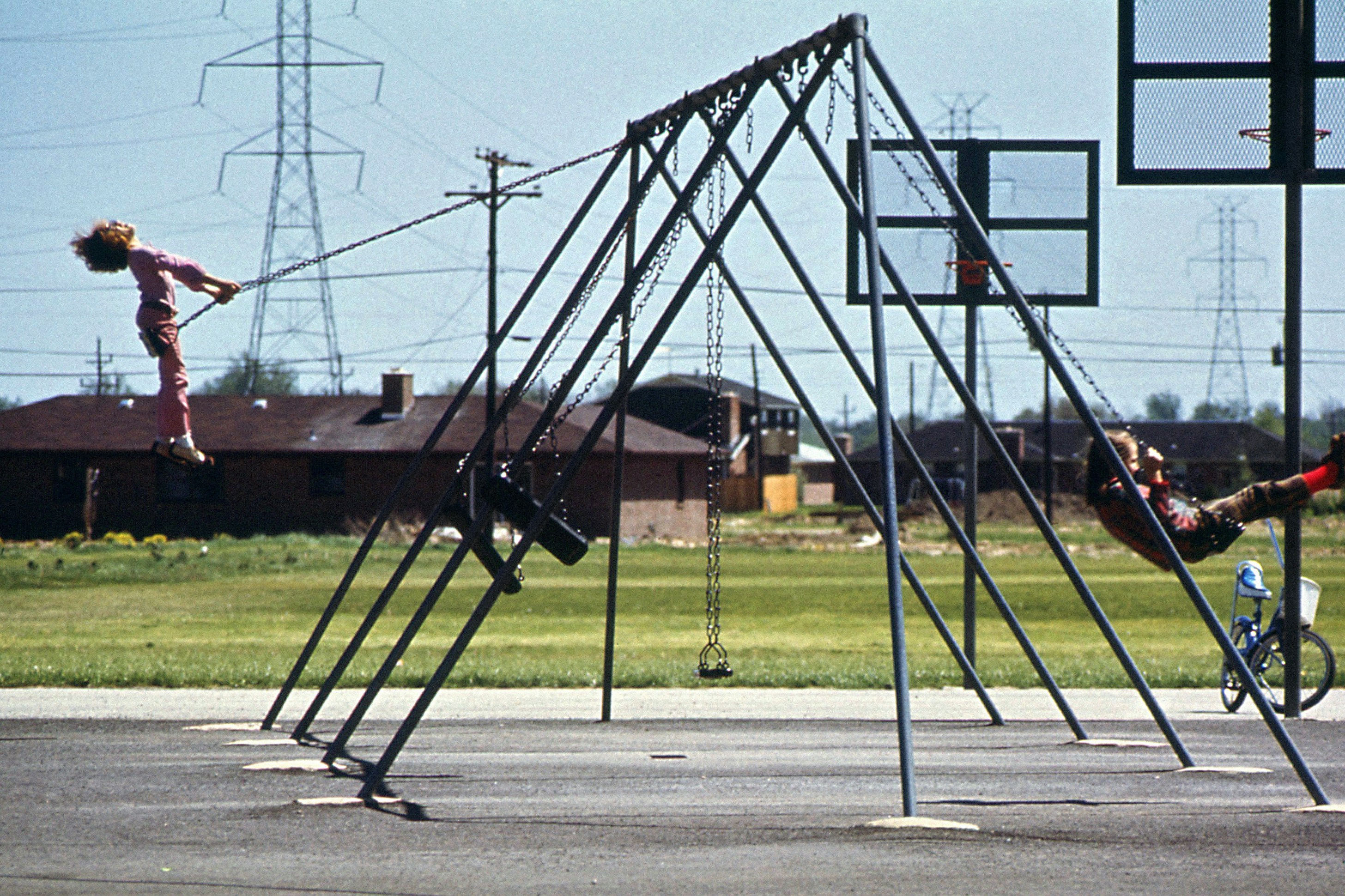 a group of people riding on top of a metal structure, May 1973: Children on swings behind Smith elementary school, Columbus (Declan Haun / Documerica)