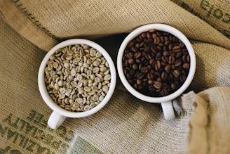 two white cups filled with coffee beans sitting on top of a couch