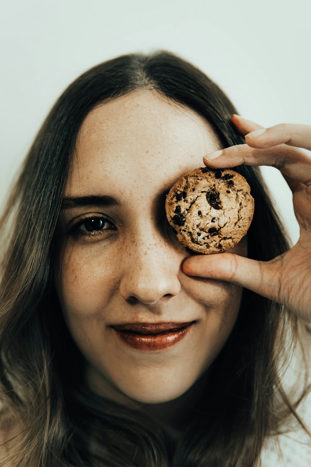 a woman holding a chocolate chip cookie up to her eye