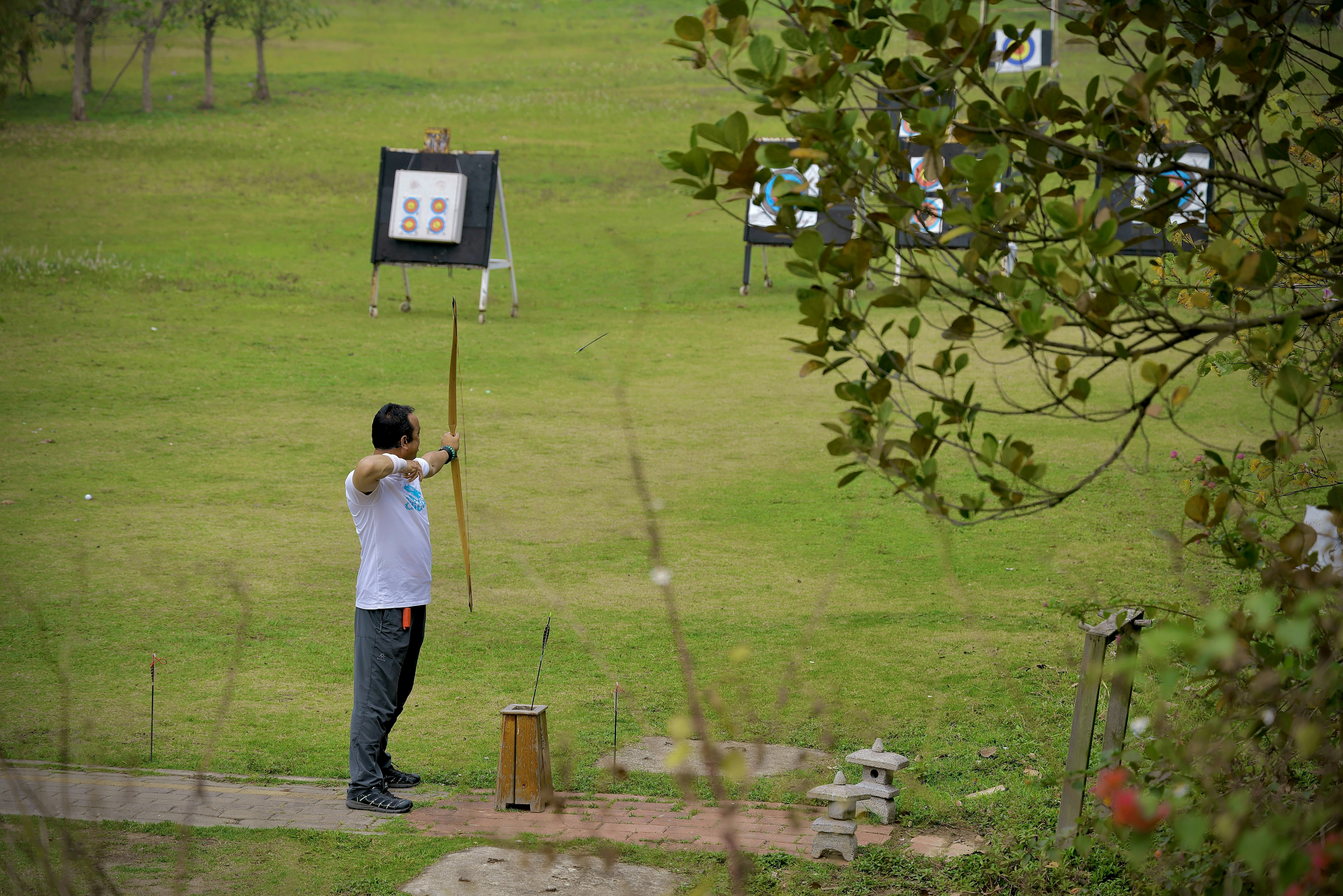 a man holding a baseball bat on top of a lush green field, Saturday Archery Class 