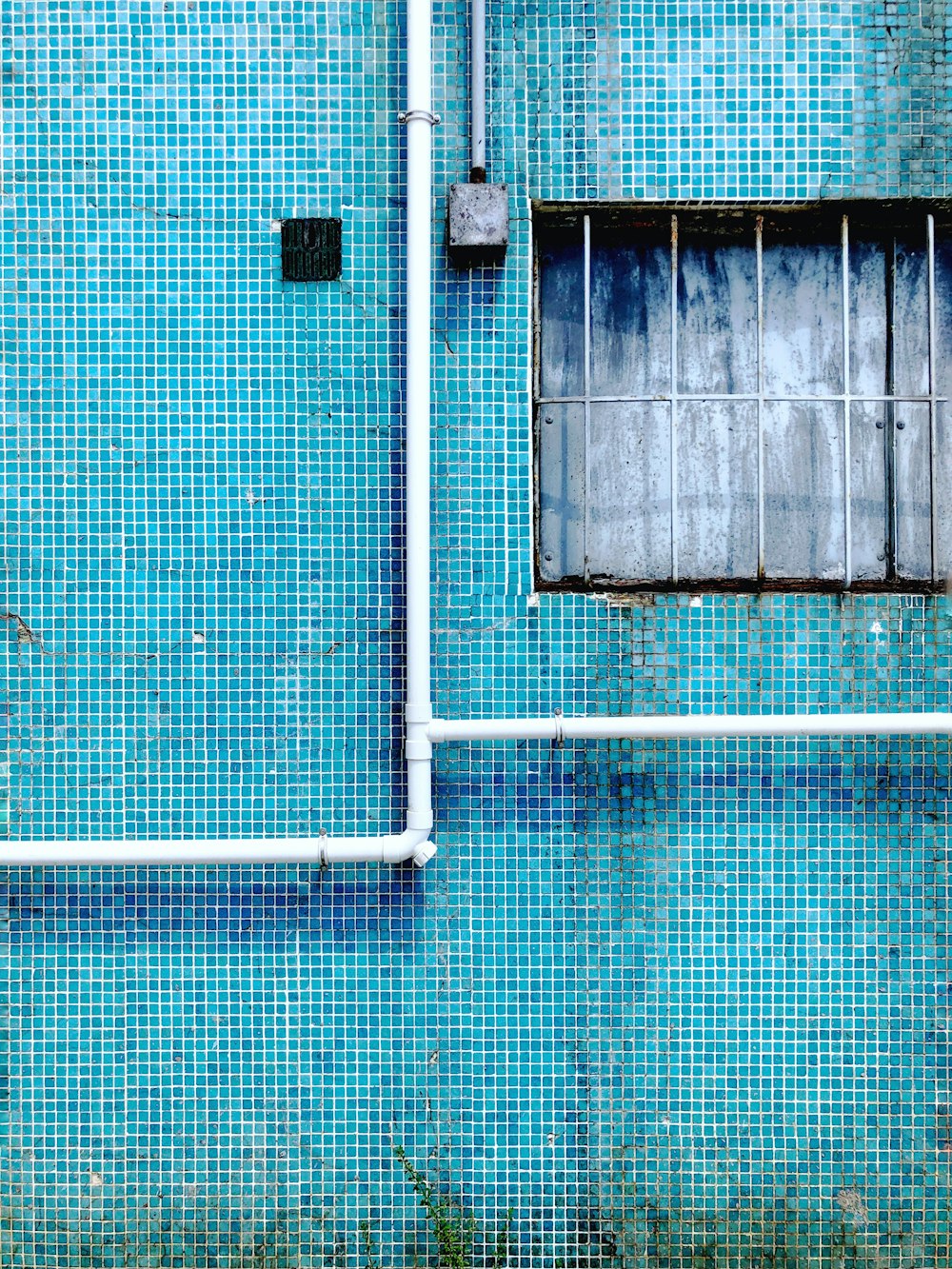 eine blaue Wand mit Fenster und Rohren