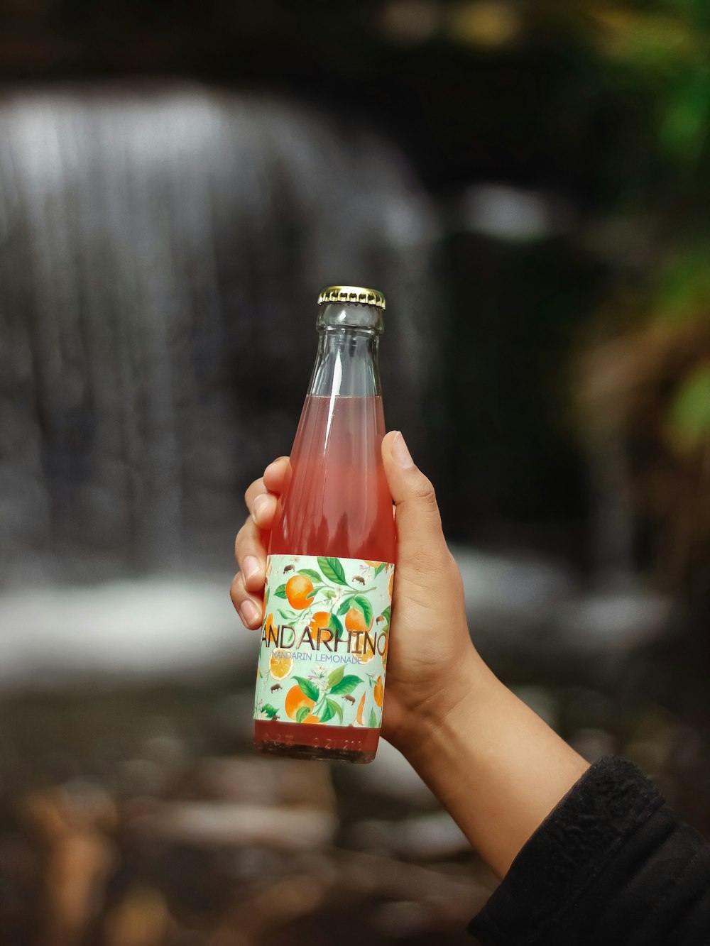 a person holding a bottle of soda in front of a waterfall