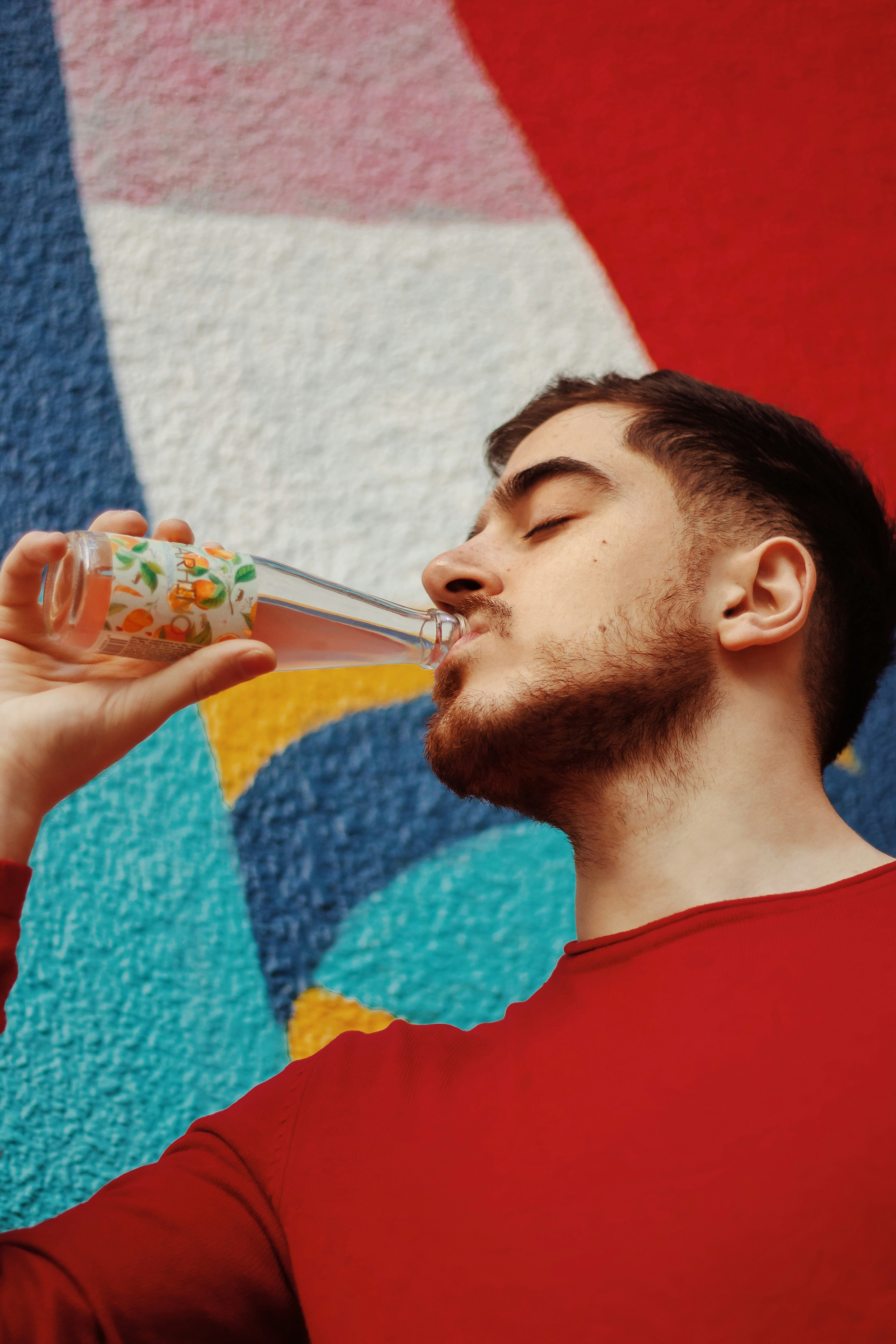 Un hombre bebiendo de un vaso frente a una pared colorida