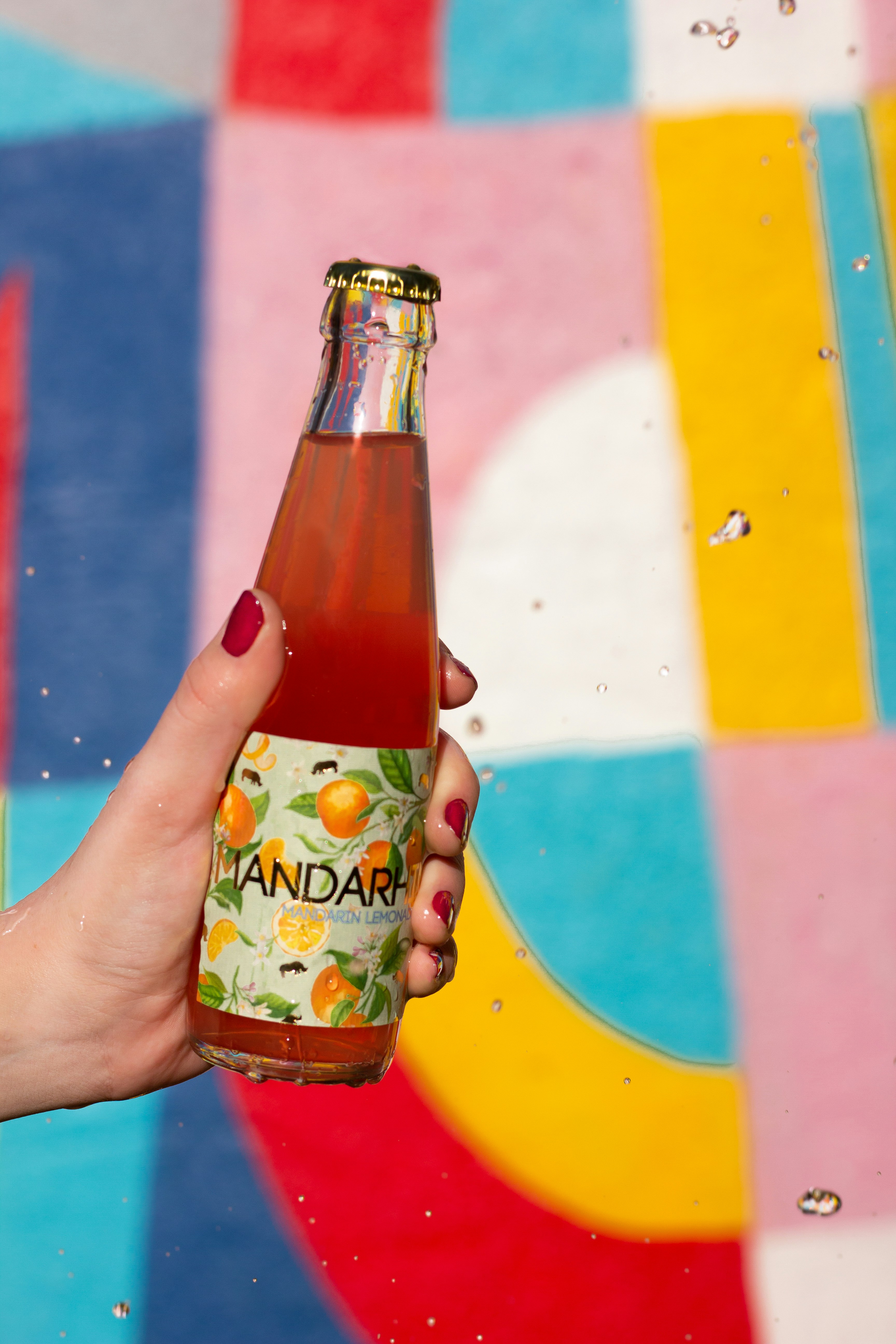 a woman holding a bottle of soda in front of a colorful wall
