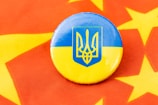 A round badge featuring the blue and yellow flag of Ukraine with the national coat of arms is placed on a red fabric decorated with yellow stars.