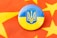 A round badge featuring the blue and yellow flag of Ukraine with the national coat of arms is placed on a red fabric decorated with yellow stars.