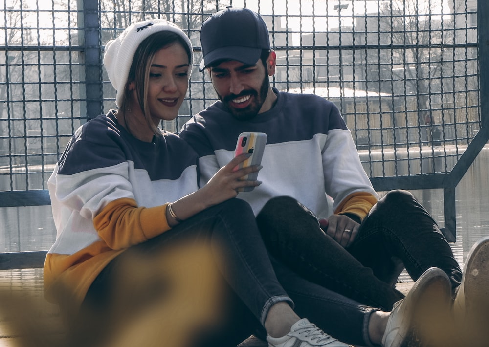 a man and woman sitting on the ground looking at a cell phone