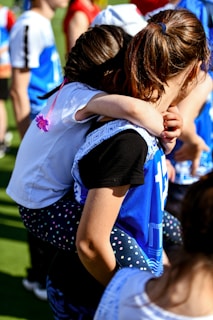two young girls hugging each other on a field