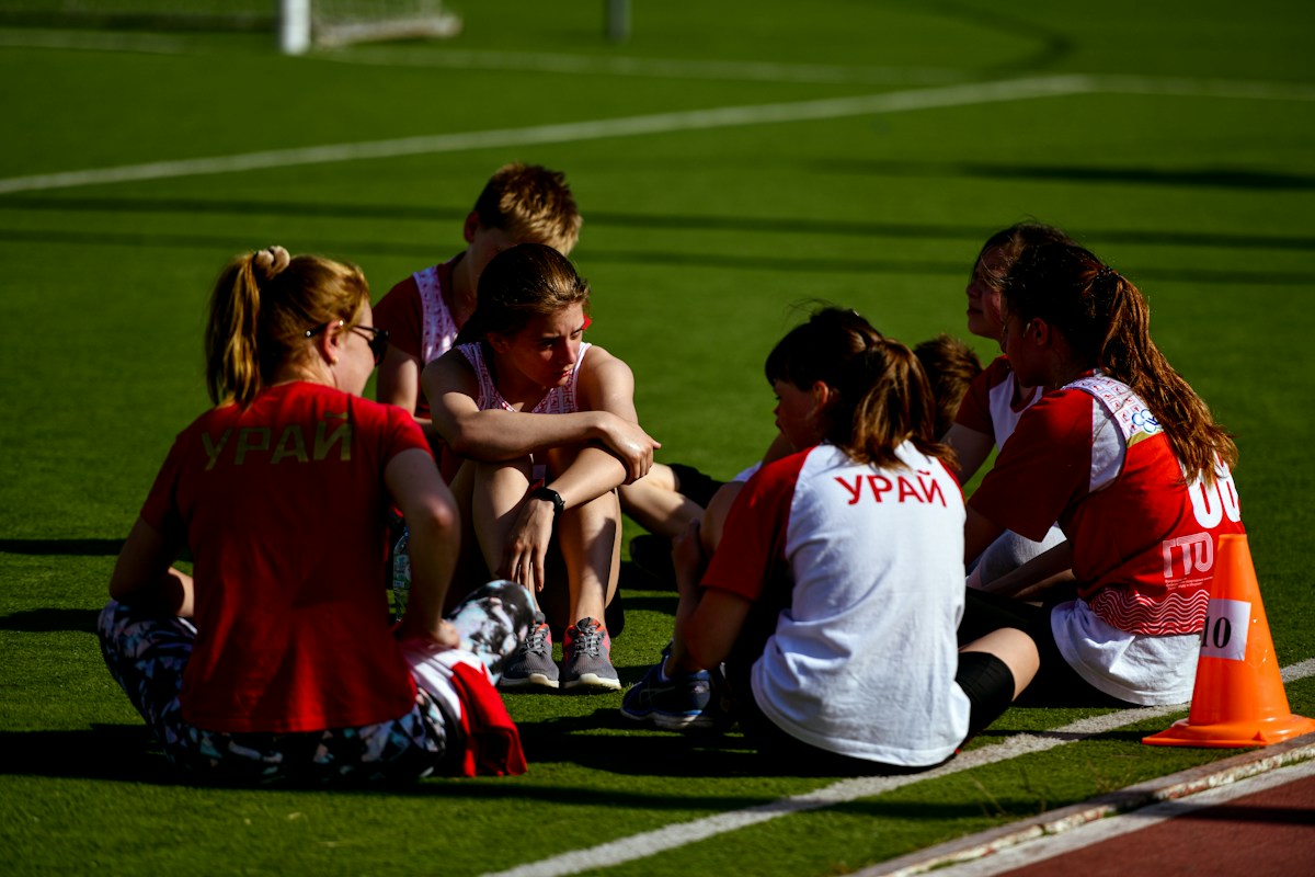 A group of young women soccer players sitting together on a field, engaging in team bonding activities for sports teams.
