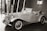 An elegant vintage car is displayed indoors, featuring a classic design with chrome accents and distinctive curves. The convertible has a prominent front grille and spoked wheels. The background includes modern architecture and a sign with Chinese characters.