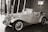An elegant vintage car is displayed indoors, featuring a classic design with chrome accents and distinctive curves. The convertible has a prominent front grille and spoked wheels. The background includes modern architecture and a sign with Chinese characters.