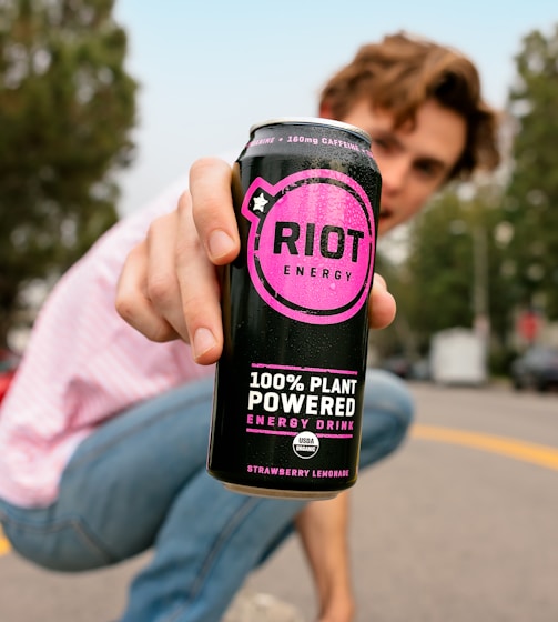 a man squatting down holding a can of riot energy