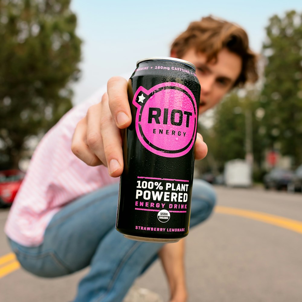 a man squatting down holding a can of riot energy