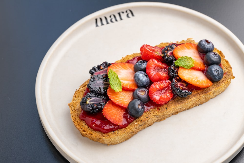 a white plate topped with a piece of bread covered in fruit