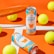 Two cans of Positive Energy drink in a vibrant setting, surrounded by several yellow tennis balls on an orange and white background. An orange tennis racket is positioned to the side, creating a sporty atmosphere.