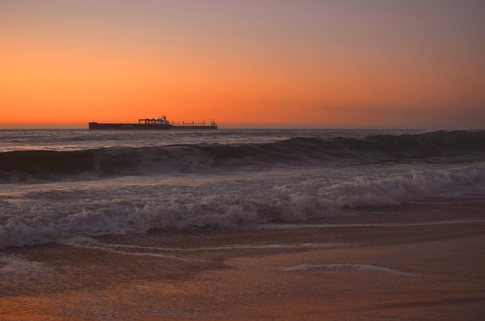 the sun is setting over the ocean with a ship in the distance