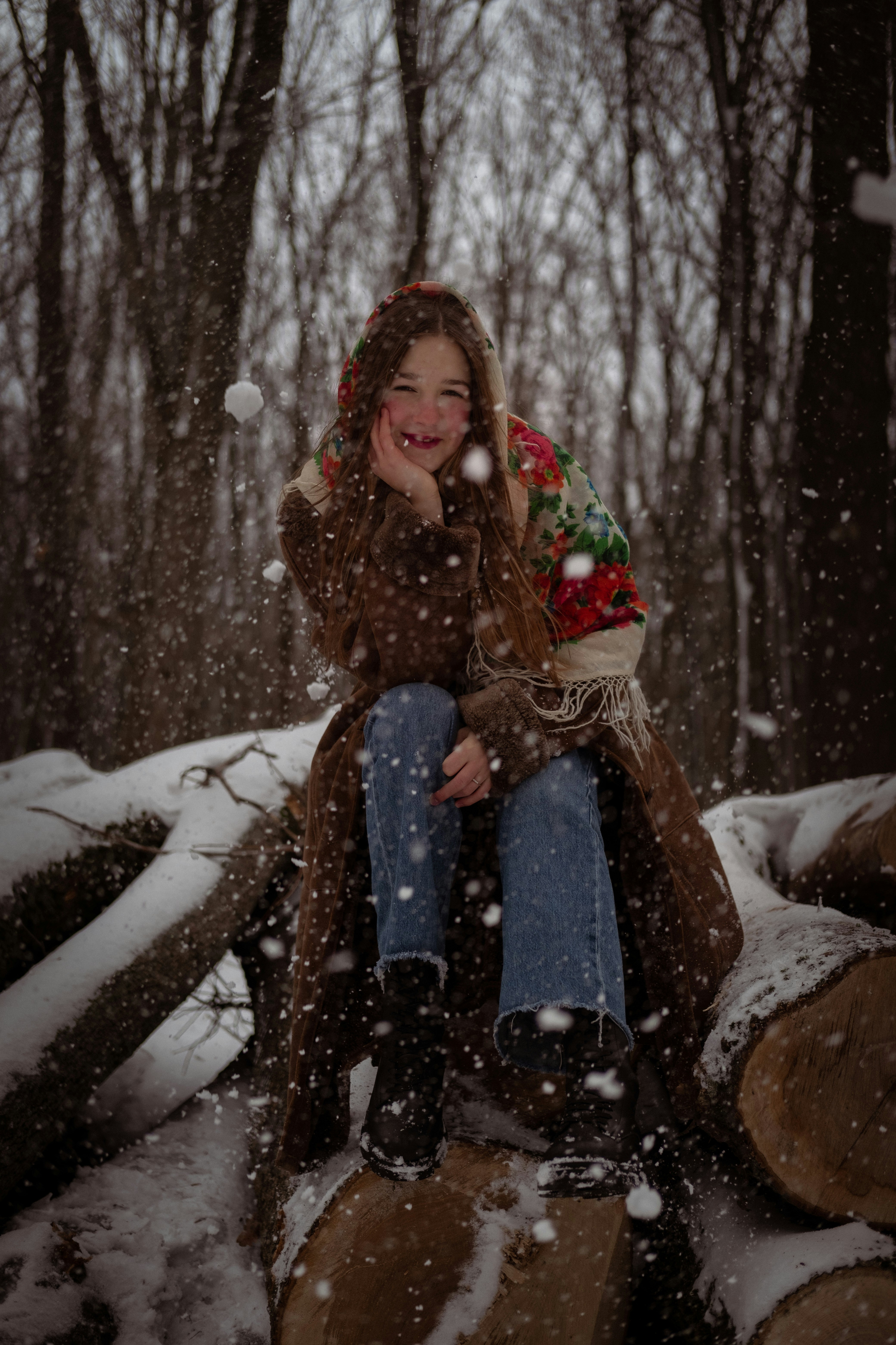 a woman sitting on top of a pile of logs in the snow