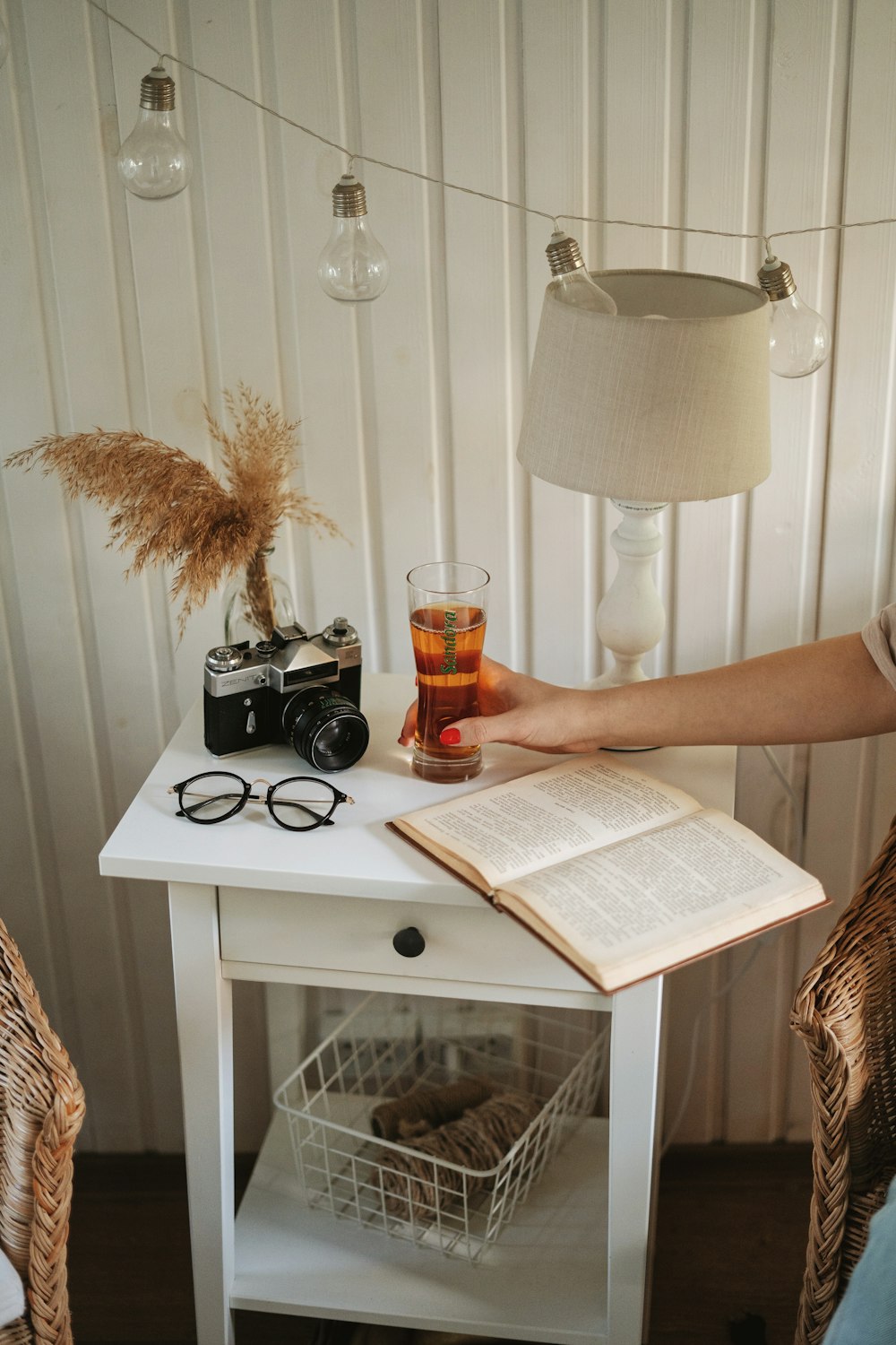 a table with a book, glasses, a camera and a lamp