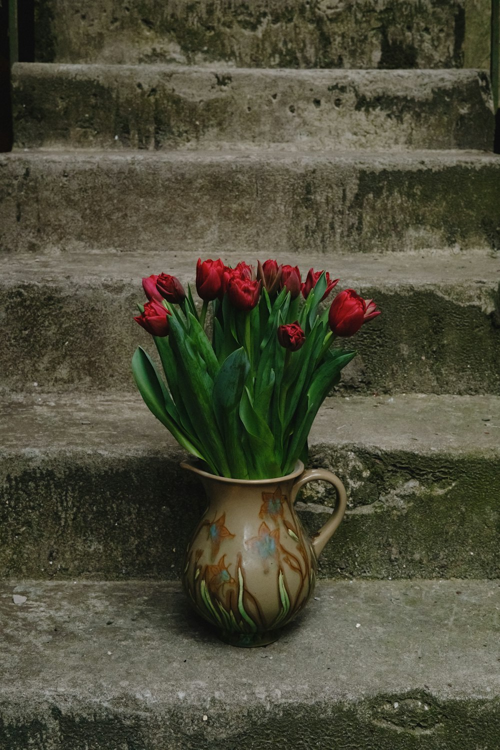 a vase filled with red flowers sitting on top of a set of steps