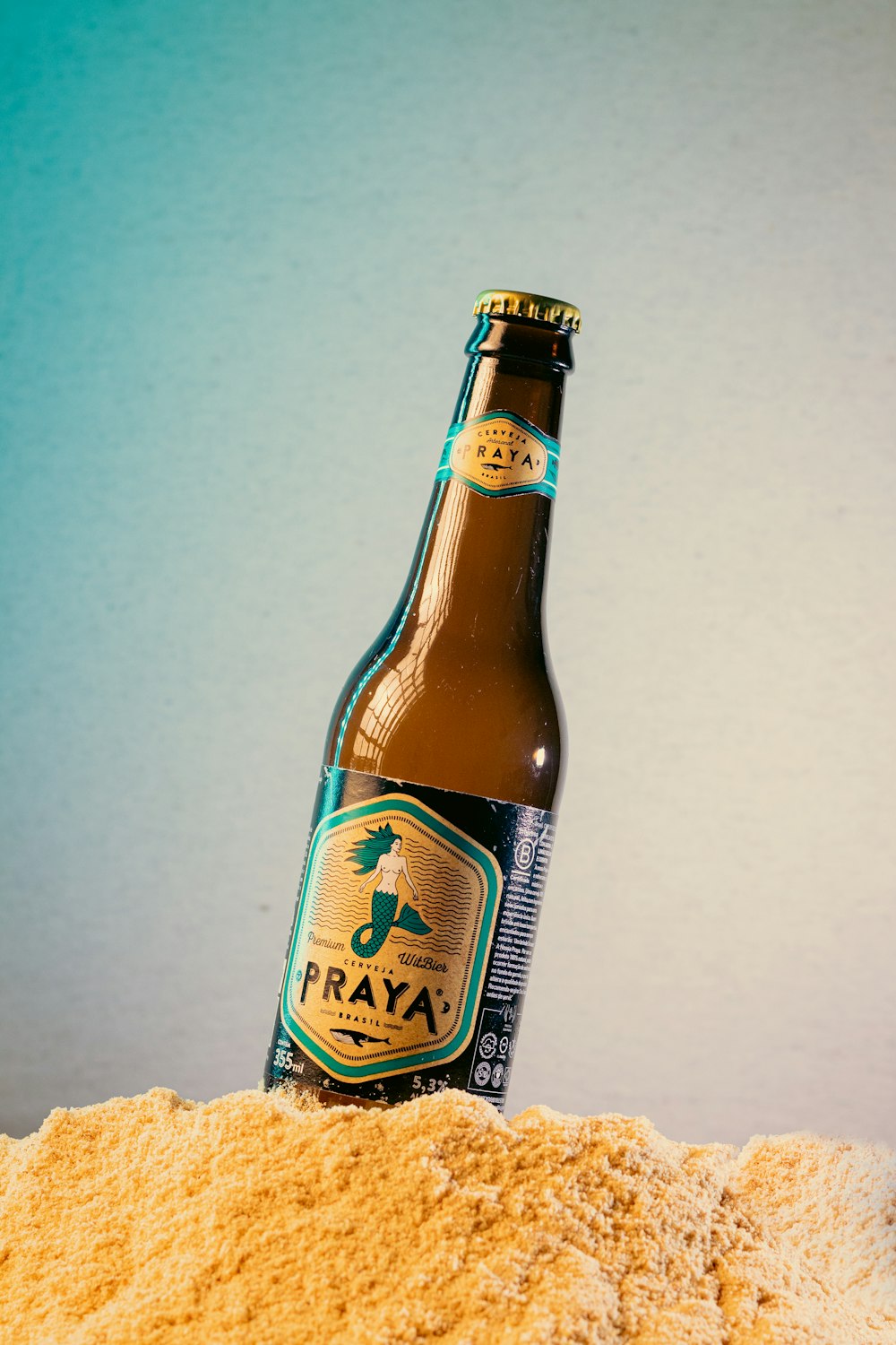 a bottle of beer sitting on top of a pile of sand
