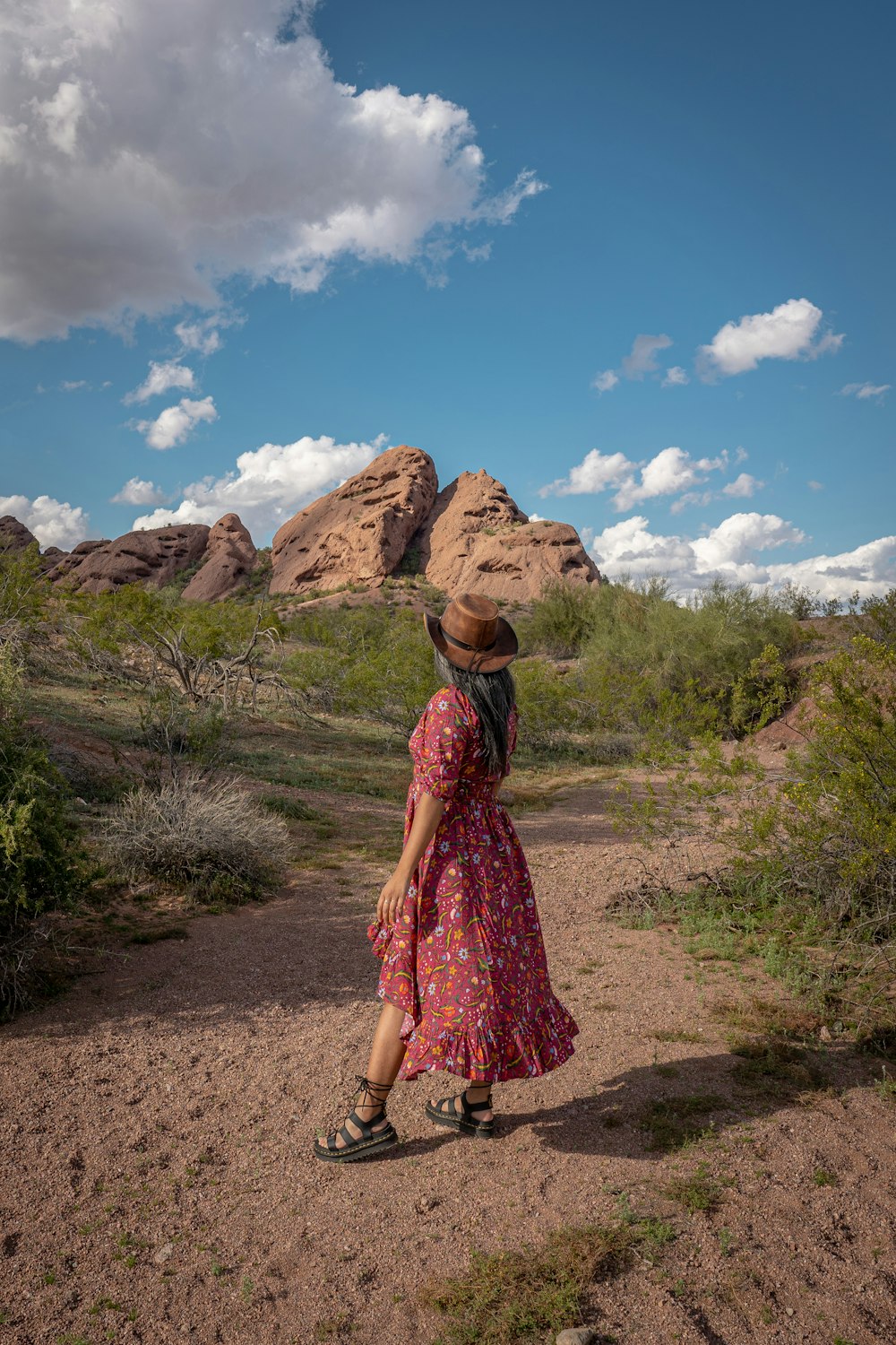 a woman in a dress and hat walking in the desert