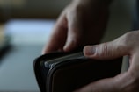 A person's hands holding a wallet, partially unzipped, with several cards visible inside.