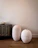 Two large, textured, white ceramic vases are placed on a wooden floor beside a dark, geometrically patterned cabinet. A small ornate vase sits on top of the cabinet, adding to the minimalist decor. The background is a plain, light-colored wall.
