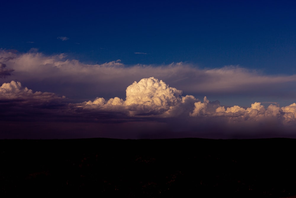 Eine große Wolke steht am Himmel über einem Hügel