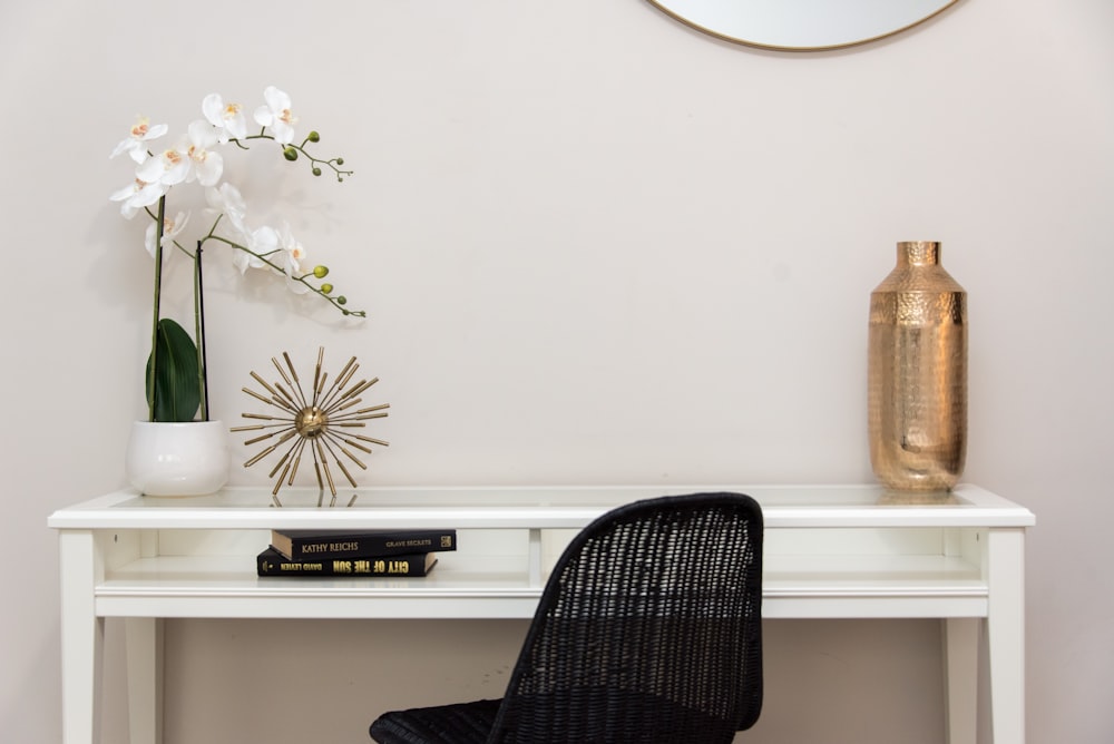 una scrivania bianca sormontata da una sedia nera e un vaso pieno di fiori