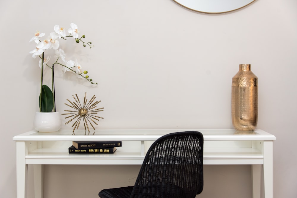 un escritorio blanco cubierto con una silla negra y un jarrón lleno de flores