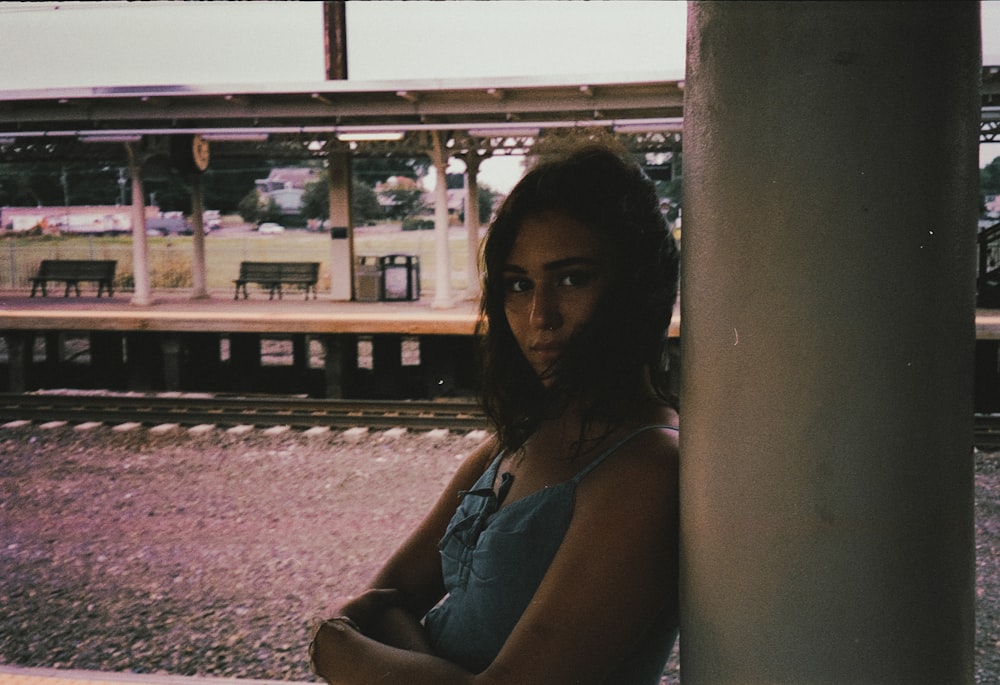 a woman leaning against a pole in front of a train station