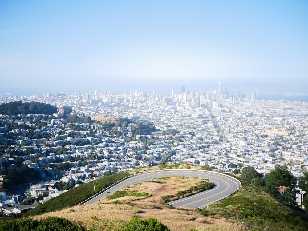 a winding road on a hill with a city in the background