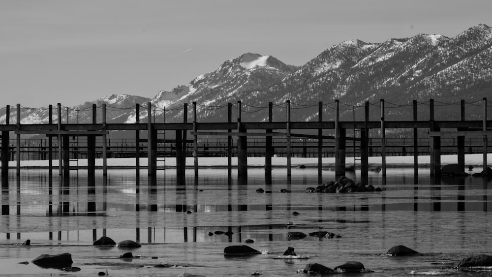a black and white photo of a pier with mountains in the background