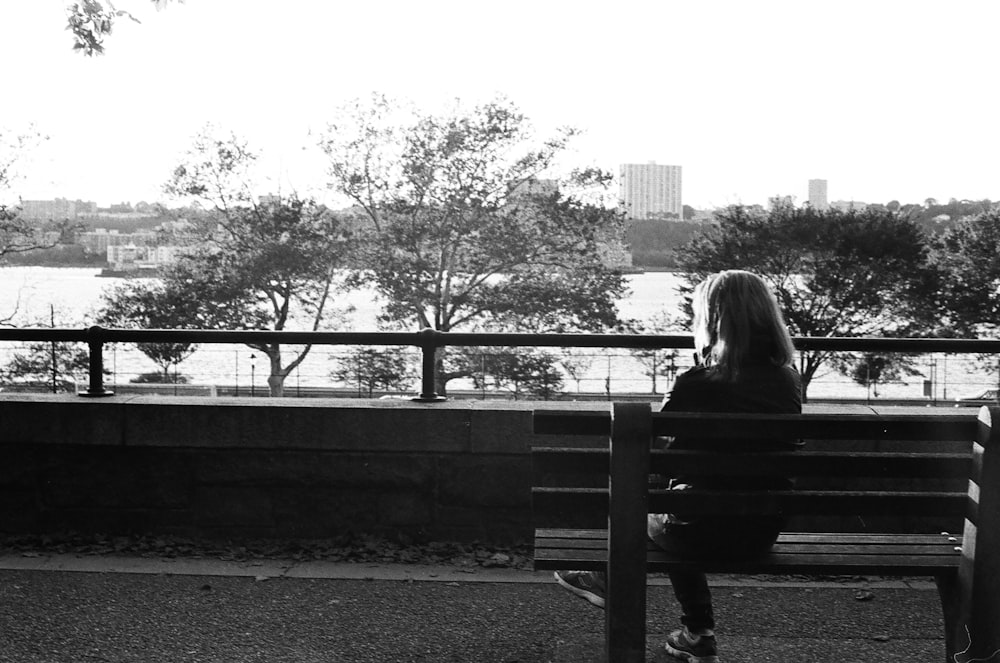 a woman is sitting on a bench looking at the water
