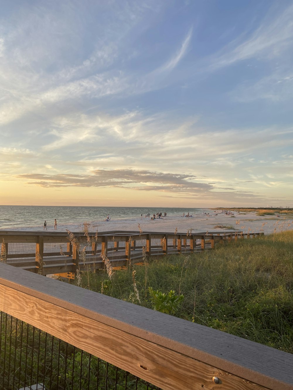 a wooden boardwalk next to the ocean at sunset