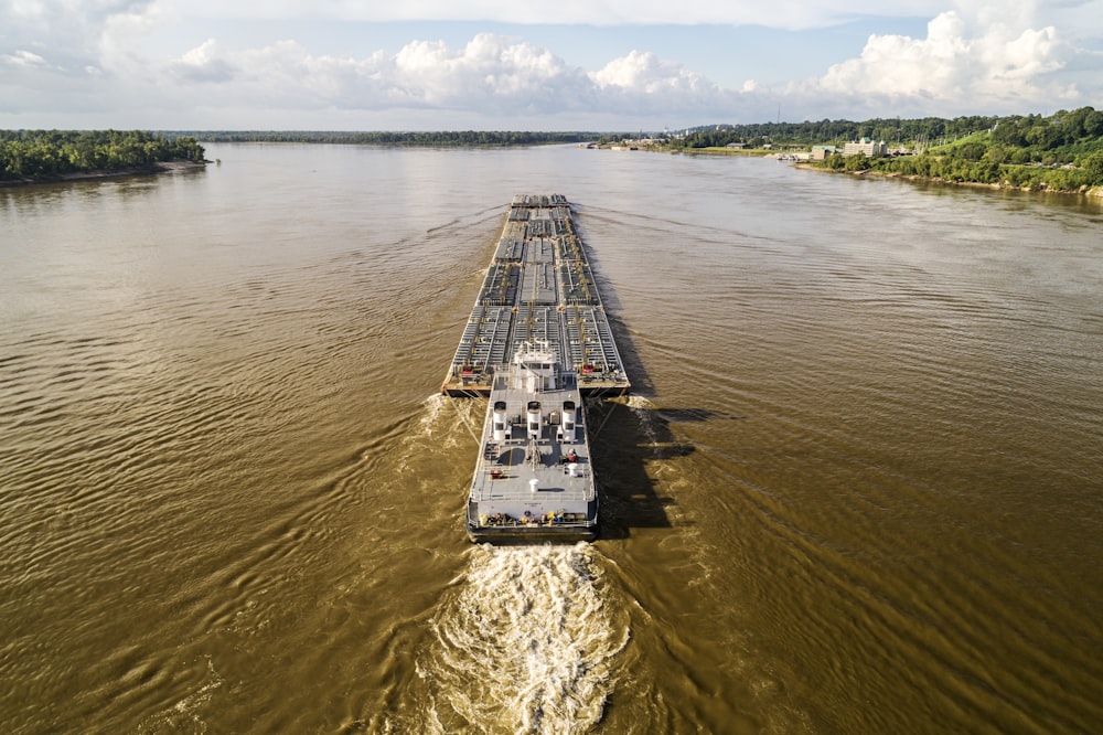 a large barge traveling down a river next to a forest