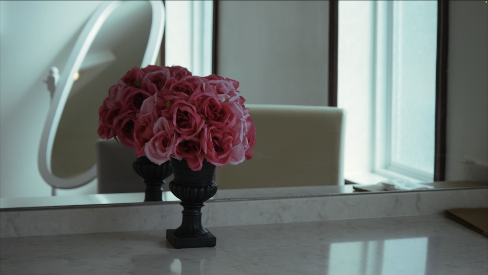 un vase de fleurs roses posé sur un comptoir devant un miroir