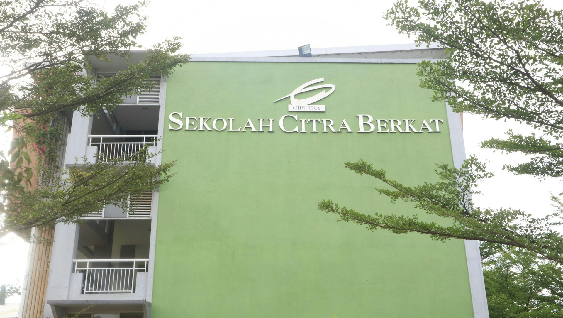 Image of the school building of SMP IT Qur'any Jaddung with its distinctive green and yellow colors under a bright sky.