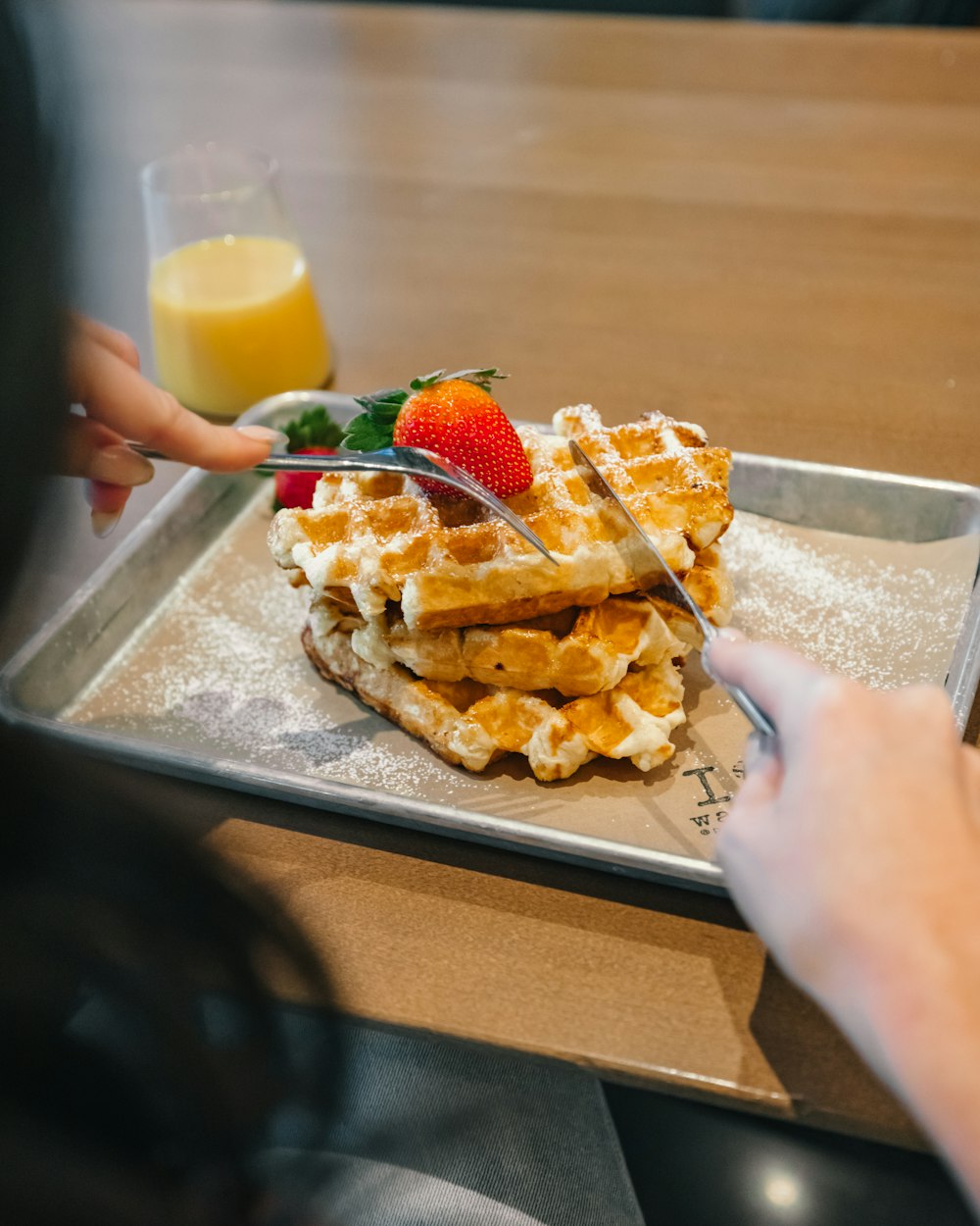 a plate of waffles with strawberries and a glass of orange juice