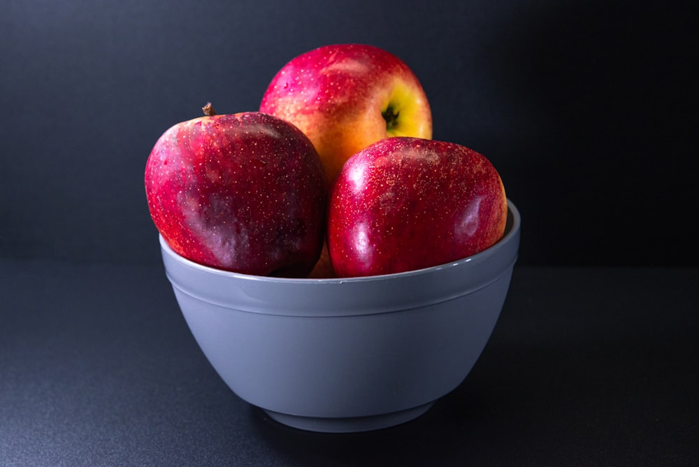 a white bowl filled with red and yellow apples